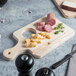 A wooden cutting board with a knife, cheese, and meat on it.