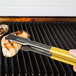 A person holding Vollrath Jacob's Pride tongs with a yellow Kool Touch handle over a grill.
