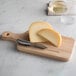 A wooden cutting board with a cheese knife and cheese on it.