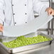 A chef using a Flexsil high-heat silicone lid to cover a metal steam table pan of green beans.