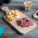 A Choice wooden serving and cutting board with cheese and meat on it.
