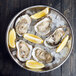 A stainless steel American Metalcraft seafood tray with oysters on ice and lemon wedges.