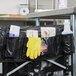 A black bag with yellow gloves and cleaning supplies on a white Rubbermaid laundry cart.