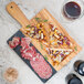An American Metalcraft olive wood and black marble serving board with sliced meat, cheese, and bread on it.