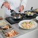 A chef using a Choice Butane Omelet / Pasta Station to cook pasta in a pan on a counter.