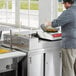 A man cooking food on an Avantco stainless steel omelet / pasta station base in a commercial kitchen.