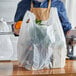 A person holding a white Choice medium-duty plastic bag full of groceries.