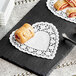 A heart-shaped white paper doily on a table with pastries on a plate.