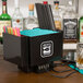 A black Chef Master bar caddy on a counter with straws, a bottle, and a drink inside.