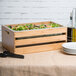 An American Metalcraft bamboo wood crate with a salad inside next to plates and a bottle of oil.