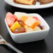 A Libbey square white porcelain bowl filled with fruit with a fork next to it.
