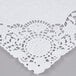 A white floral lace paper placemat on a gray surface.