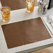 A brown scalloped paper placemat on a table with glasses of ice tea.