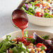 A bowl of salad with Hidden Valley Raspberry Vinaigrette being poured over it.