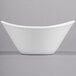 A close-up of a Libbey Aluma White Porcelain Infinity Bowl with a curved edge on a gray surface.
