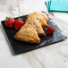 A Elite Global Solutions faux black slate melamine serving board with three scones and strawberries on a counter.