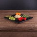 An Elite Global Solutions faux black slate melamine serving board with vegetables on a wood table.