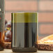 An Arcoroc green wine bottle tumbler filled with wine on a table next to a bottle of wine.