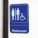 A blue and white rectangular Thunder Group restroom sign with a person and a wheelchair.