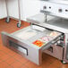 An Avantco stainless steel refrigeration pan divider bar in a kitchen drawer with food inside.