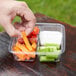 A hand putting a carrot and celery into a Fabri-Kal Greenware plastic deli container.