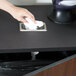 A hand holding a white tissue wiping a Vollrath stainless steel in-counter trash chute.
