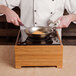 A chef using a Cal-Mil bamboo countertop induction cooker to cook food in a pan.