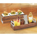 A Cal-Mil walnut wood and chrome reversible riser on a table with a tray of food and drinks.