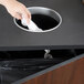 A hand putting a tissue in a Vollrath in-counter trash chute.
