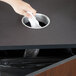 A hand throwing a tissue into a Vollrath stainless steel in-counter trash chute.