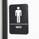 A black and white Thunder Group ADA men's restroom sign with a man symbol.