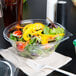 A salad in a Dart plastic bowl with a fork on a counter.