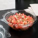 A bowl of salsa with a Dart plastic tamper-evident lid on a table.