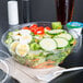 A Dart plastic deli bowl filled with salad and a fork on a napkin.