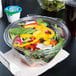 A salad in a Dart plastic container with a flat lid and a drink.