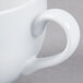 A close-up of a white Tuxton porcelain cappuccino cup with a handle.