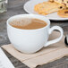 A Tuxton porcelain white cappuccino cup filled with coffee with foam and cookies on a table.