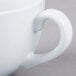A close-up of a white Tuxton cappuccino cup with a handle.