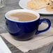 A Tuxton cobalt blue cappuccino cup filled with brown liquid on a table.