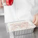 A chef sprinkles sprinkles on a Durable Packaging square cake in a foil pan.