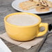 A Tuxton saffron cappuccino cup filled with a foamy drink on a wooden table with cookies and a spoon.