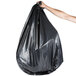 A hand holding a black Berry low density heavy-duty trash bag.