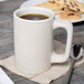 A Tuxton Texan eggshell white mug filled with brown liquid on a table with cookies.