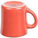 A close-up of a small orange Tuxton china mug with a white handle.