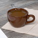 A brown Tuxton mahogany espresso cup filled with coffee on a table.