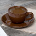 A brown Tuxton mahogany cappuccino cup of coffee on a saucer.