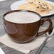 A mahogany Tuxton cappuccino cup filled with coffee on a table with cookies and a spoon.