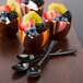 A WNA Comet black plastic tasting spoon with a chocolate cup filled with fruit.
