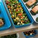 A blue Cambro market pan on a counter with food in it, including green beans, broccoli, and potatoes.