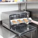 A woman putting a tray of cookies into a Waring countertop convection oven.